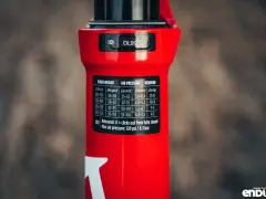 Czerwiony amortyzator Rock Shox z naklejką zawierającą tabelę ciśnień i ustawień powrotu dla różnych wag rowerzysty.
