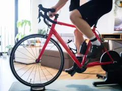 Intensywny trening na trenażerze kolarskim w domu. Czerwony rower, sportowiec w spodenkach i koszulce, butelki z wodą.