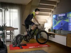 Mężczyzna ćwiczy na rowerze stacjonarnym, korzystając z aplikacji do trenażera, która wyświetla wirtualną trasę na dużym ekranie telewizora.