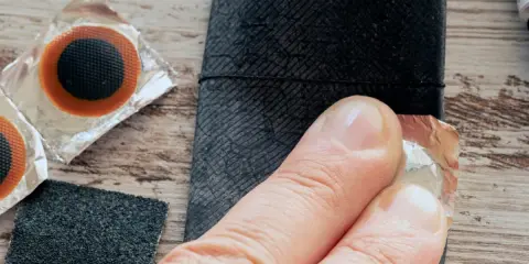 Łatka do dętki rowerowej z przerzutką w piaście. Dłoń przygotowuje łatkę do przyklejenia.
