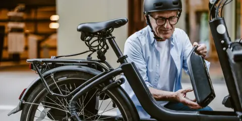 Starszy pan w kasku montuje baterię do swojego roweru 26 cali. To zestaw elektryczny do roweru, który ułatwi mu jazdę.