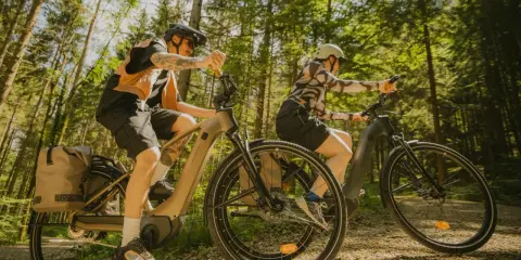 Dwie osoby na rowerach elektrycznych przemierzają leśną ścieżkę. Różne rodzaje rowerów elektrycznych pozwalają na komfortowe wycieczki.