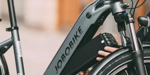 Ręce wyjmujące czarną baterię z ramy roweru elektrycznego JOBORBIKE.