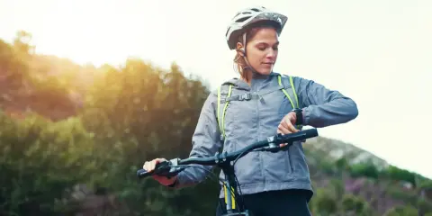 Kobieta w kasku sprawdza na zegarku spalone kalorie podczas jazdy na rowerze w słoneczny dzień.