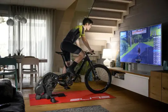 Mężczyzna ćwiczy na rowerze stacjonarnym, korzystając z aplikacji do trenażera, która wyświetla wirtualną trasę na dużym ekranie telewizora.