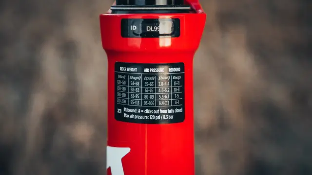 Czerwiony amortyzator Rock Shox z naklejką zawierającą tabelę ciśnień i ustawień powrotu dla różnych wag rowerzysty.