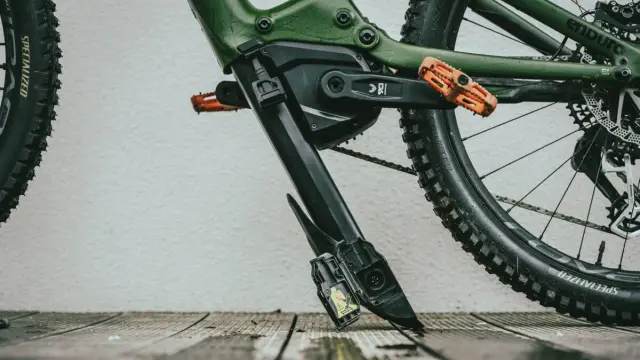 Zielony rower elektryczny z pomarańczowymi pedałami. Widoczny mechanizm, który ułatwia zrozumienie, jak wyjąć baterię z roweru elektrycznego.