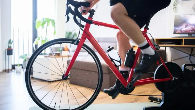 Intensywny trening na trenażerze kolarskim w domu. Czerwony rower, sportowiec w spodenkach i koszulce, butelki z wodą.