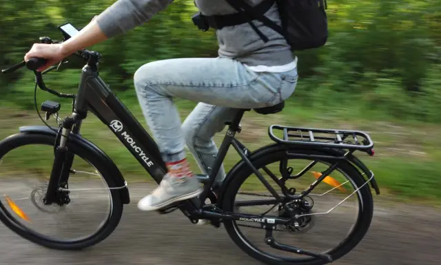 Osoba na rowerze elektrycznym Molicyle z amortyzacją pokonuje leśną ścieżkę.