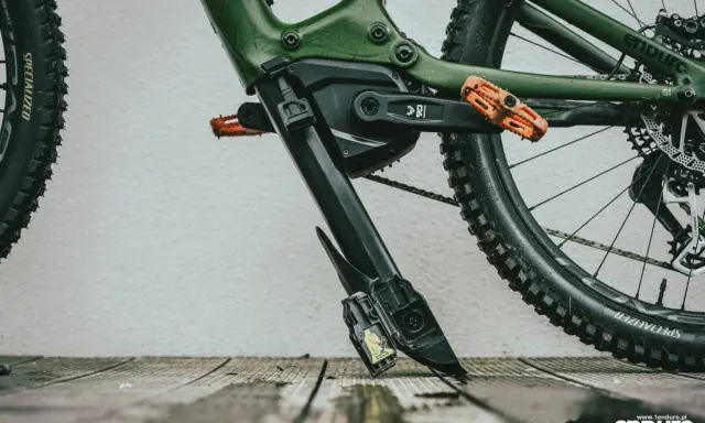 Zielony rower elektryczny z pomarańczowymi pedałami. Widoczny mechanizm, który ułatwia zrozumienie, jak wyjąć baterię z roweru elektrycznego.