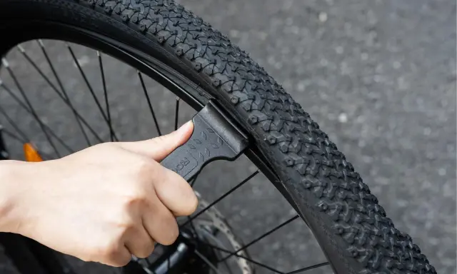 Dłoń używa czarnej łyżki do opon rowerowych, aby zdjąć oponę z obręczy. To proste narzędzie, które ułatwia wymianę dętki.