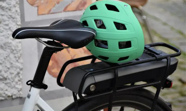 Zielony kask na bagażniku roweru elektrycznego, obok siodełka. Baterie do rowerów elektrycznych są gotowe do długiej podróży.