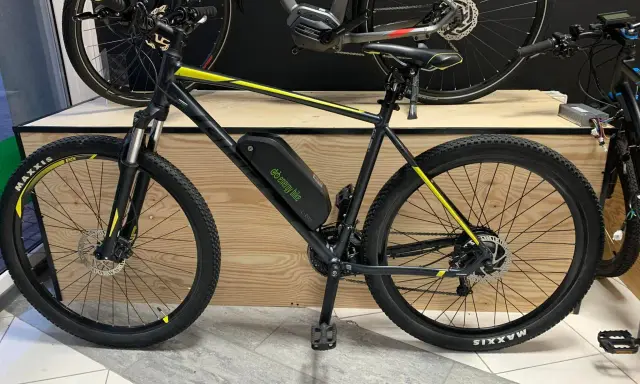 Czarny rower z żółtymi akcentami, wyposażony w baterię i silnik, prezentuje tani zestaw do konwersji roweru na elektryczny.