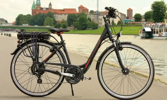 Rower z widocznym bagażnikiem i baterią, gotowy do konwersji na elektryczny. W tle zamek Królewski na Wawelu.