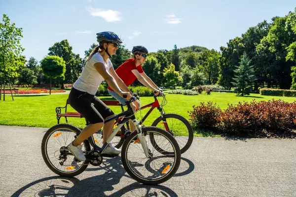Dwie osoby na rowerach cieszą się piękną pogodą w parku. To pokazuje, co daje jazda na rowerze: aktywność, relaks i kontakt z naturą.