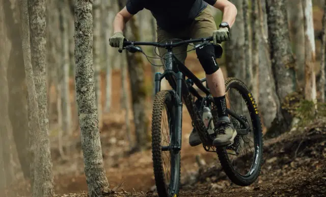 Rowerzysta w kasku i ochraniaczach pokonuje leśny szlak na rowerze górskim, jednym z wielu rodzajów rowerów do jazdy terenowej.