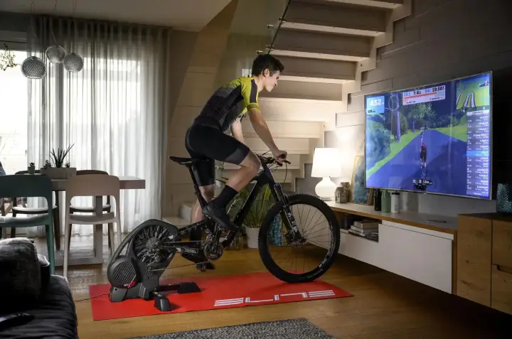 Mężczyzna ćwiczy na rowerze stacjonarnym, korzystając z aplikacji do trenażera, która wyświetla wirtualną trasę na dużym ekranie telewizora.